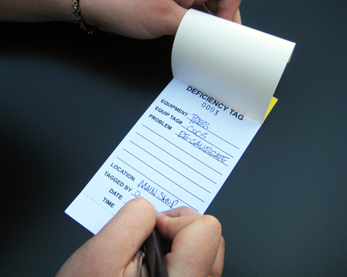 An image of a deficiency tag with hand written information being entered on the inner carbon copy.