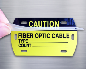 An image of a fiber optic telecom cable tag reading, "Caution, Fiber Optic Cable". Tag is rectangular with rounded ends and has a clear, self-laminating cover and elongated slots for application the cables. Colors are black on yellow.