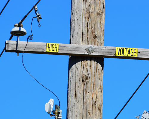 A yellow plastic cross arm sign affixed to a wooden utility pole.